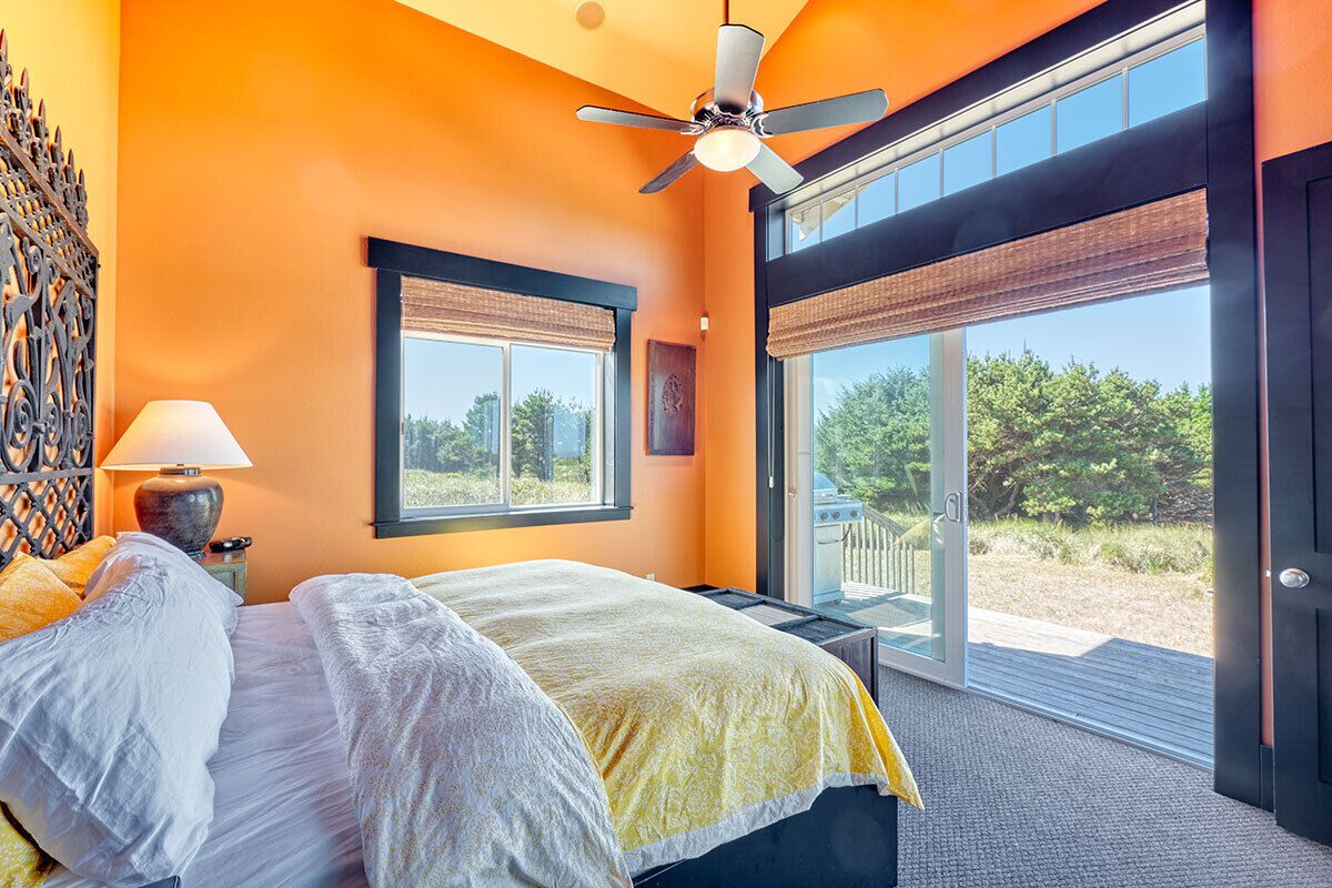 Ein Schlafzimmer mit einem Bett, einem Deckenventilator, einem Fenster mit Jalousien und Blick ins Freie.