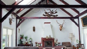 Un salon spacieux doté d’une cheminée, de poutres en bois et d’une tête de cerf accrochée au mur.