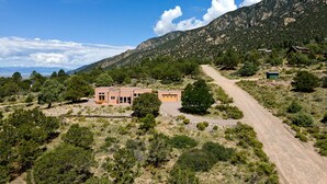 A building with a red facade, surrounded by a dry, hilly landscape with sparse vegetation and a dirt road leading to it. - Lovely Home in Crestone - Great Views! (Crestone)