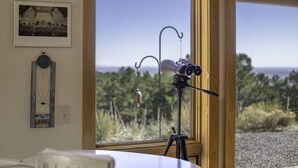 A room with a telescope on a tripod by a large window overlooking a natural landscape. - Lovely Home in Crestone - Great Views! (Crestone)