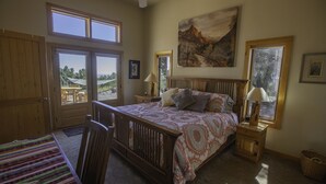 A bedroom with a large bed, a wooden crib, a window with a view, and a painting on the wall. - Lovely Home in Crestone - Great Views! (Crestone)
