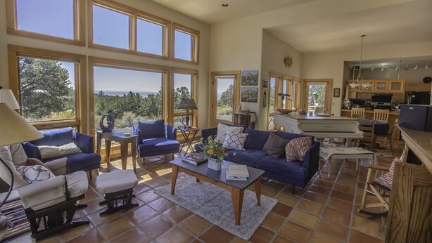 A spacious living room with large windows, a piano, and a kitchen area. - Lovely Home in Crestone - Great Views! (Crestone)