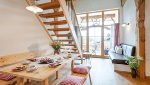 A cozy dining area with a wooden table set for a meal, a bench with checkered cushions, and a staircase leading to an upper level. - Ferienwohnung "Scheunentor", 63 qm Obergeschoss, 2 separate Schlafzimmer (Höslwang)