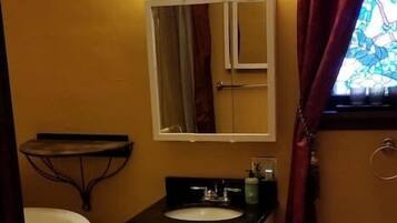 A bathroom with a white sink, mirror, and cabinet, a bathtub, and a window with curtains.