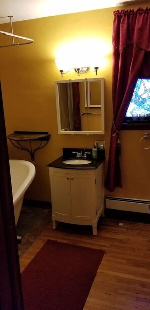 Un baño con lavamanos, espejo y mueble blanco, una bañera y una ventana con cortinas.