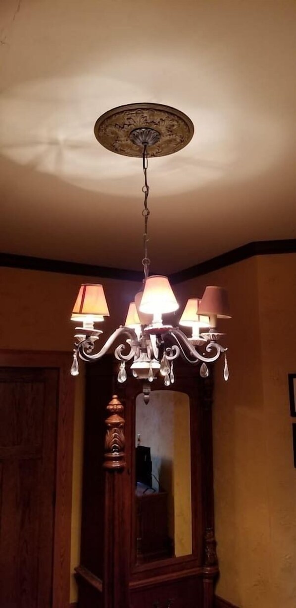 A chandelier with three lampshades hanging from a ceiling with a decorative central piece. - Historic Victorian Inn Gold Suite (Sioux Falls)