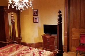 Un dormitorio con una cama con dosel, un aparador de madera, un televisor y una araña.