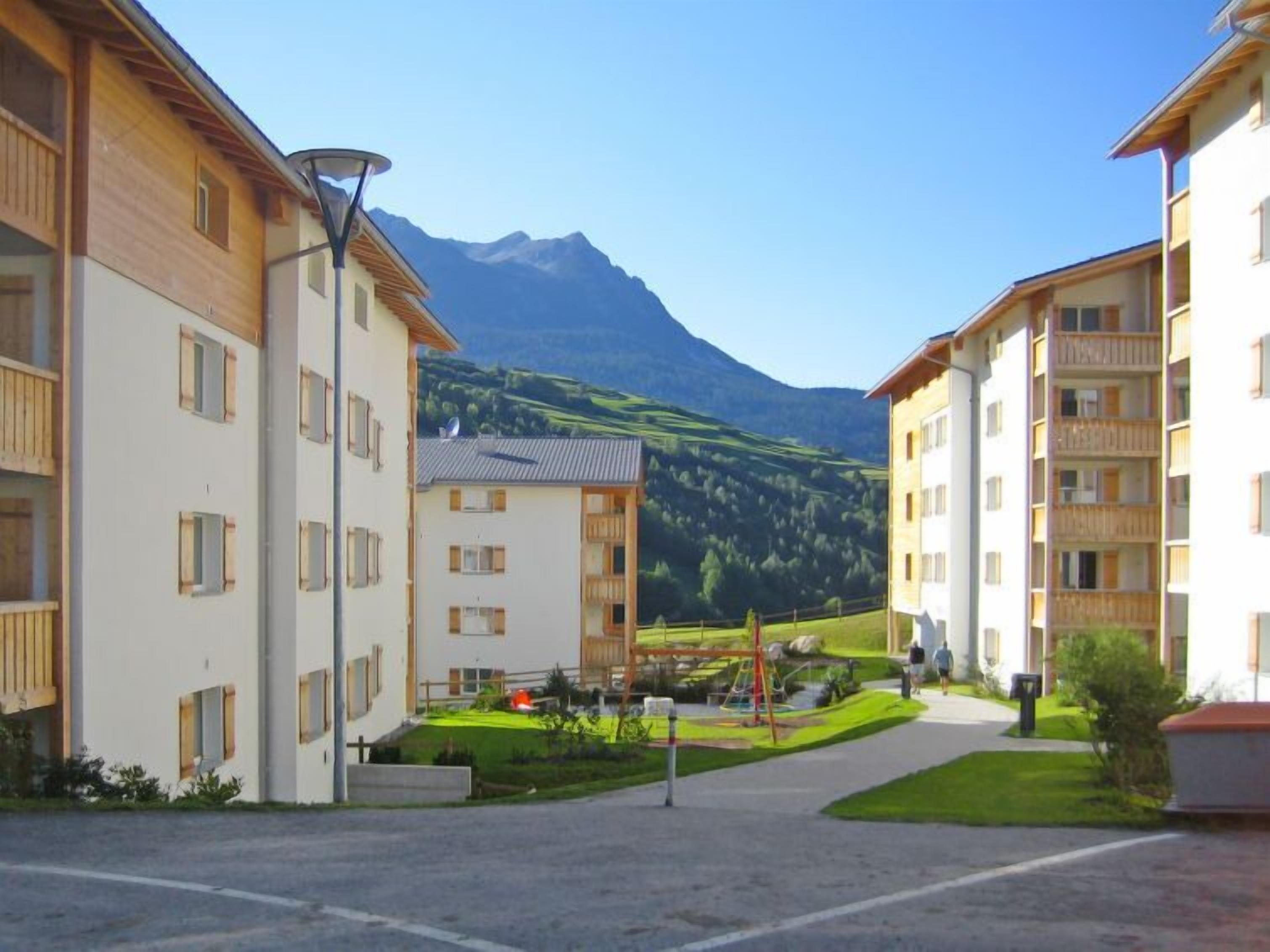 Un quartier résidentiel avec des immeubles modernes, une aire de jeux et une montagne en arrière-plan.