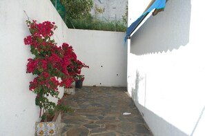 A narrow stone-paved courtyard with a white wall on one side and a blue awning on the other.