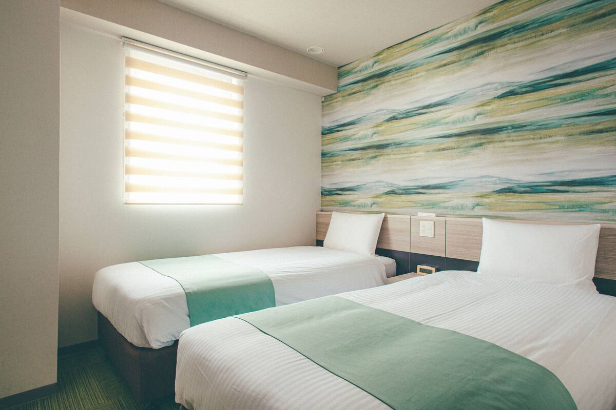 A hotel room with two beds, a large abstract painting on the wall, and a window with blinds.