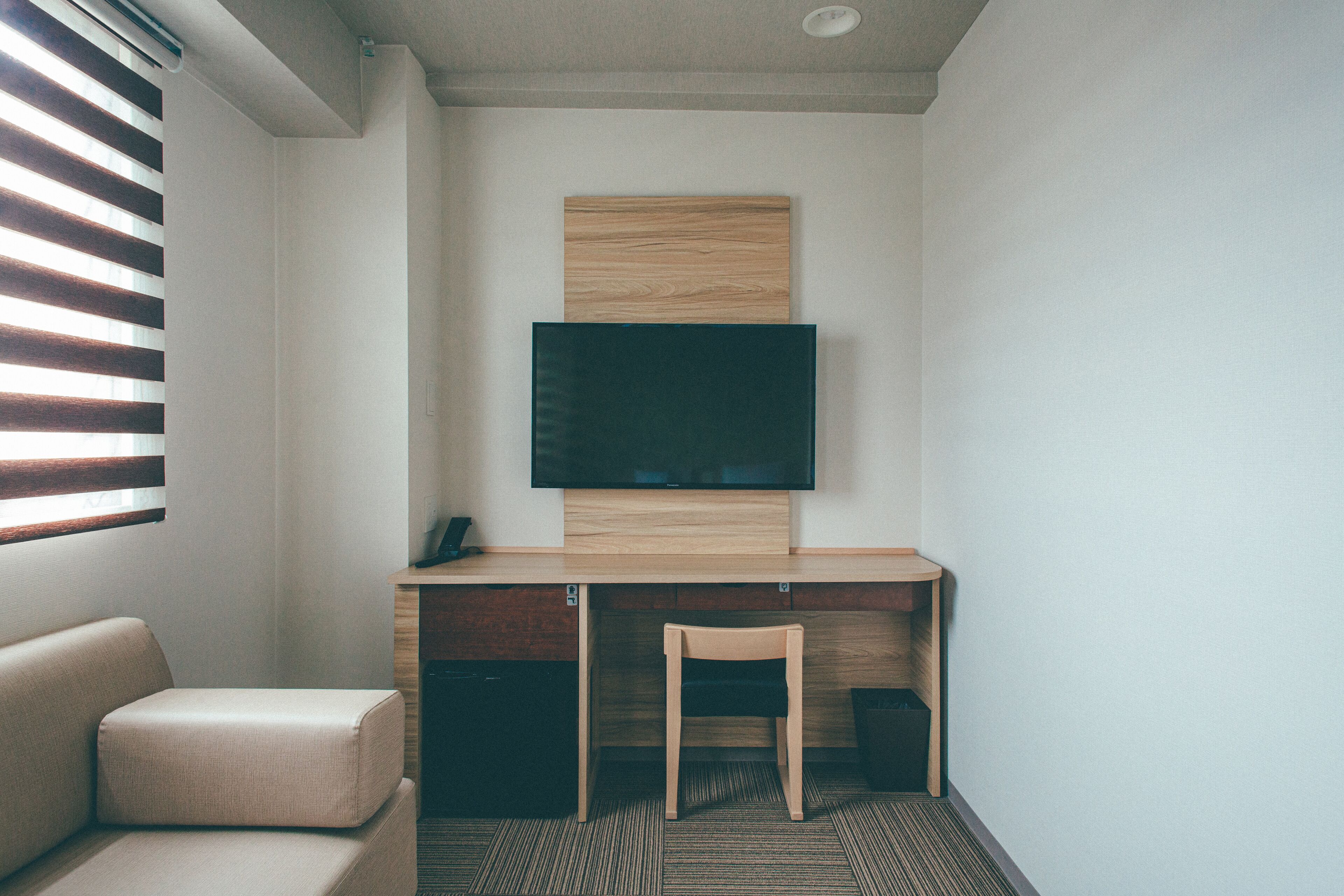 Ein modernes Hotelzimmer mit einem Holztisch, einem Flachbildfernseher, einem gepolsterten Sessel und einer Couch.