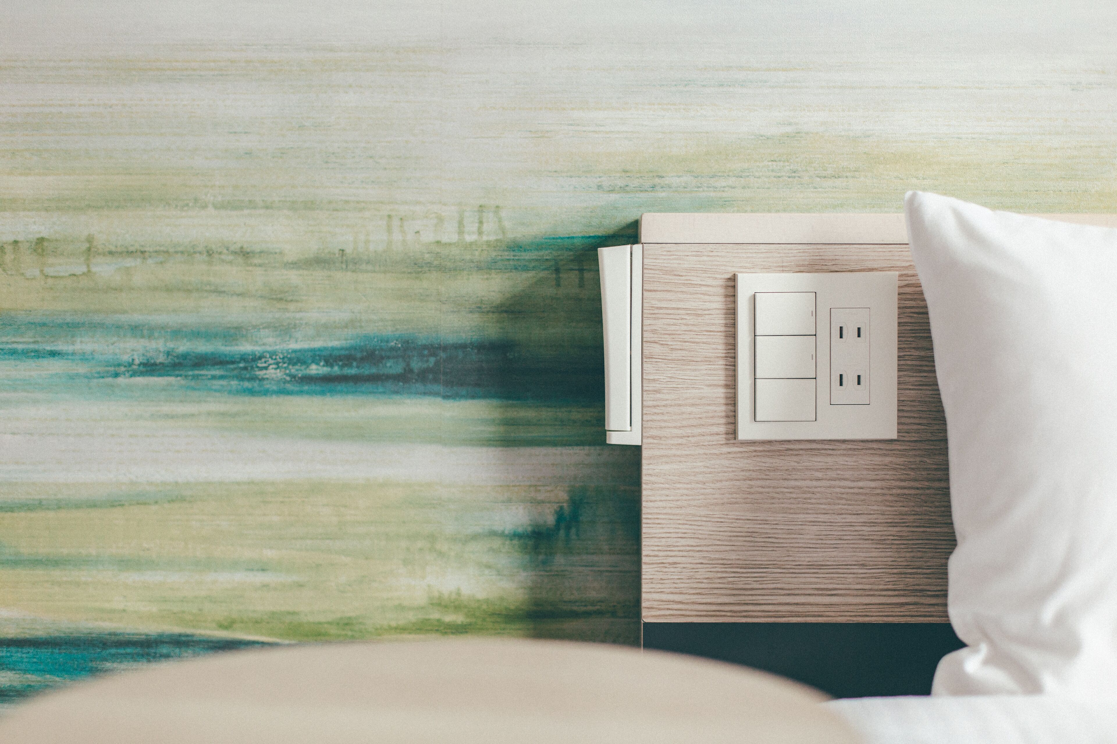 A bedroom with a wooden headboard, a white pillow, and a wall-mounted light switch.