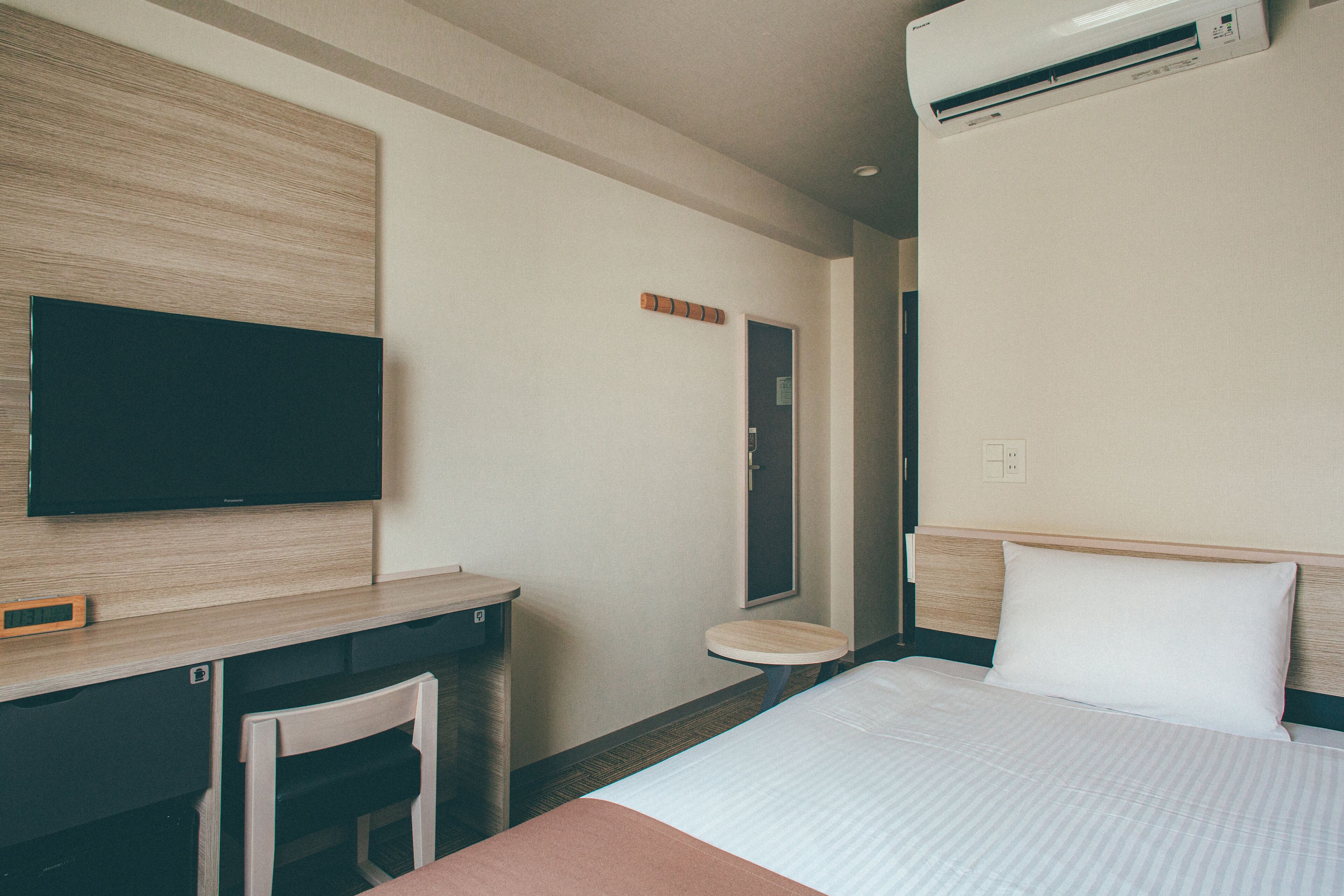Habitación de hotel con una cama, un escritorio, una silla, un televisor y un aire acondicionado.
