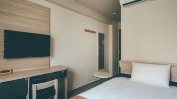 Habitación de hotel con una cama, un escritorio, una silla, un televisor y un aire acondicionado.