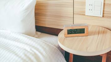 A bed with a white pillow and a round wooden nightstand with a digital clock displaying the time.