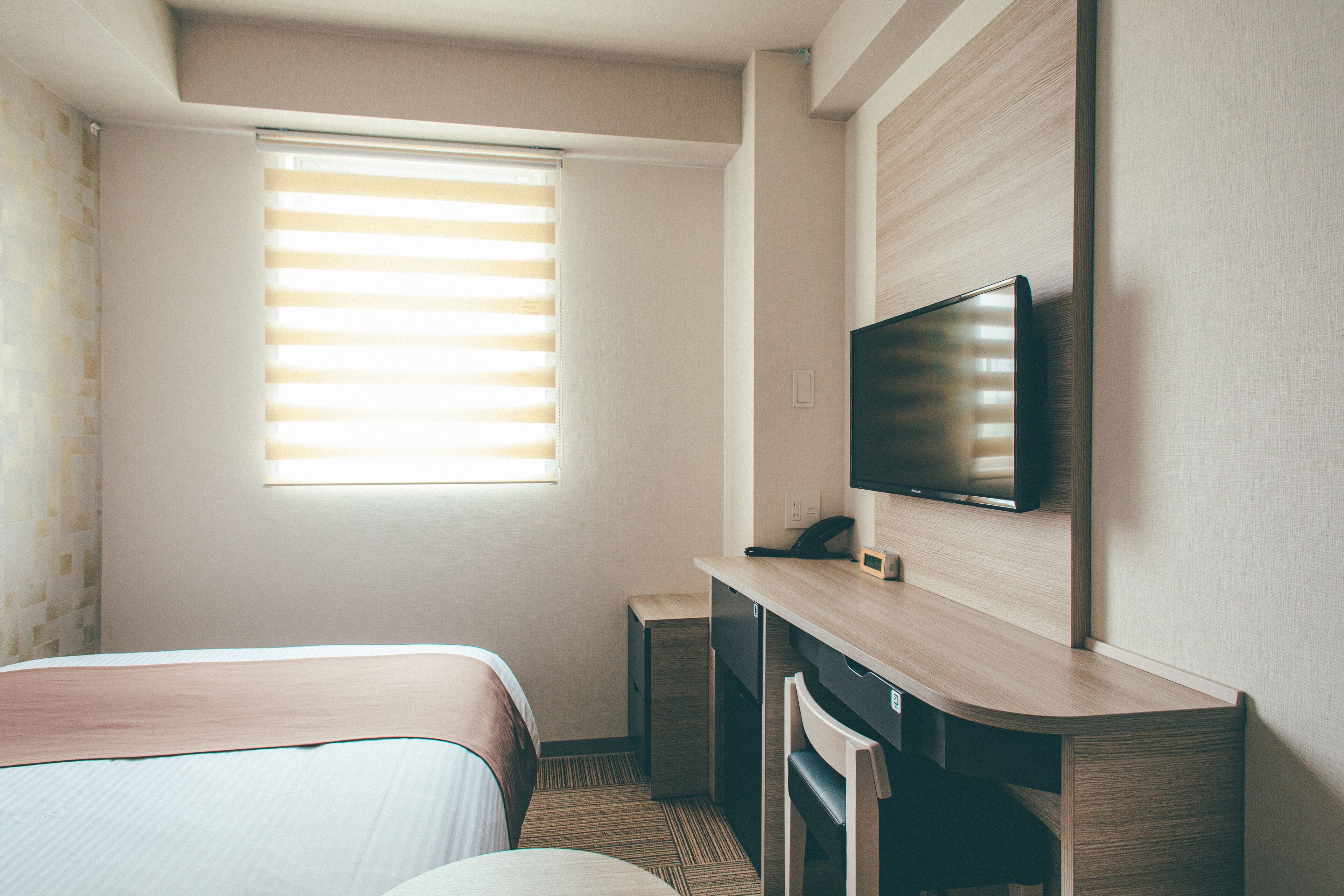 Une chambre d’hôtel avec un lit, un bureau équipé d’un ordinateur, une télévision et une fenêtre avec des stores.