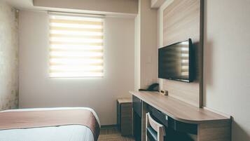 Une chambre d’hôtel avec un lit, un bureau équipé d’un ordinateur, une télévision et une fenêtre avec des stores.
