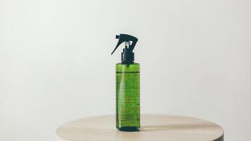 Una botella rociadora verde sobre una mesa redonda de madera, sobre un fondo liso.