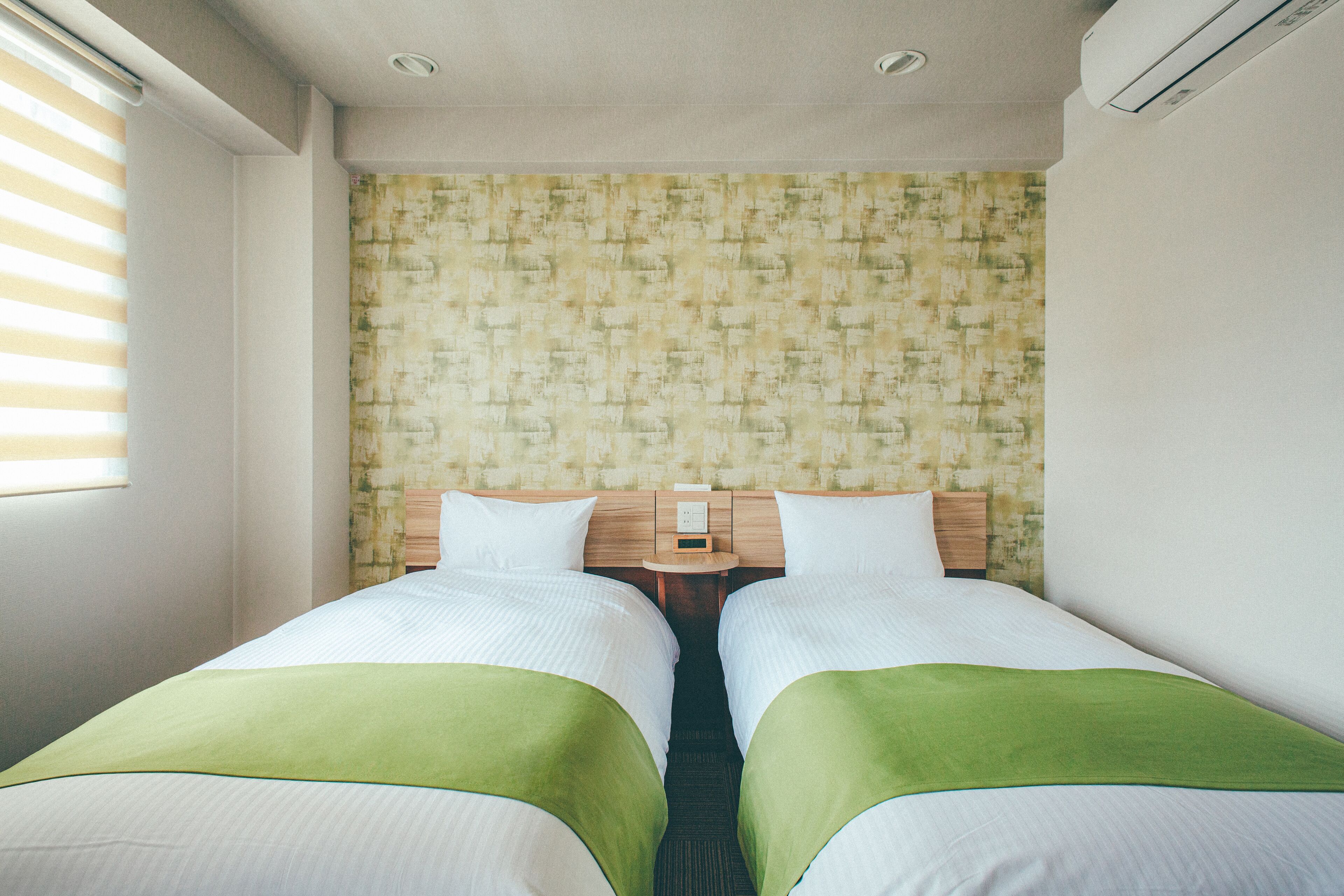 Une chambre d’hôtel avec deux lits, une tête de lit en bois, une table de chevet et un papier peint à motifs.