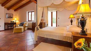 Een slaapkamer met een hemelbed, een zithoek met een stoel en tafeltje, en een raam met gordijnen.