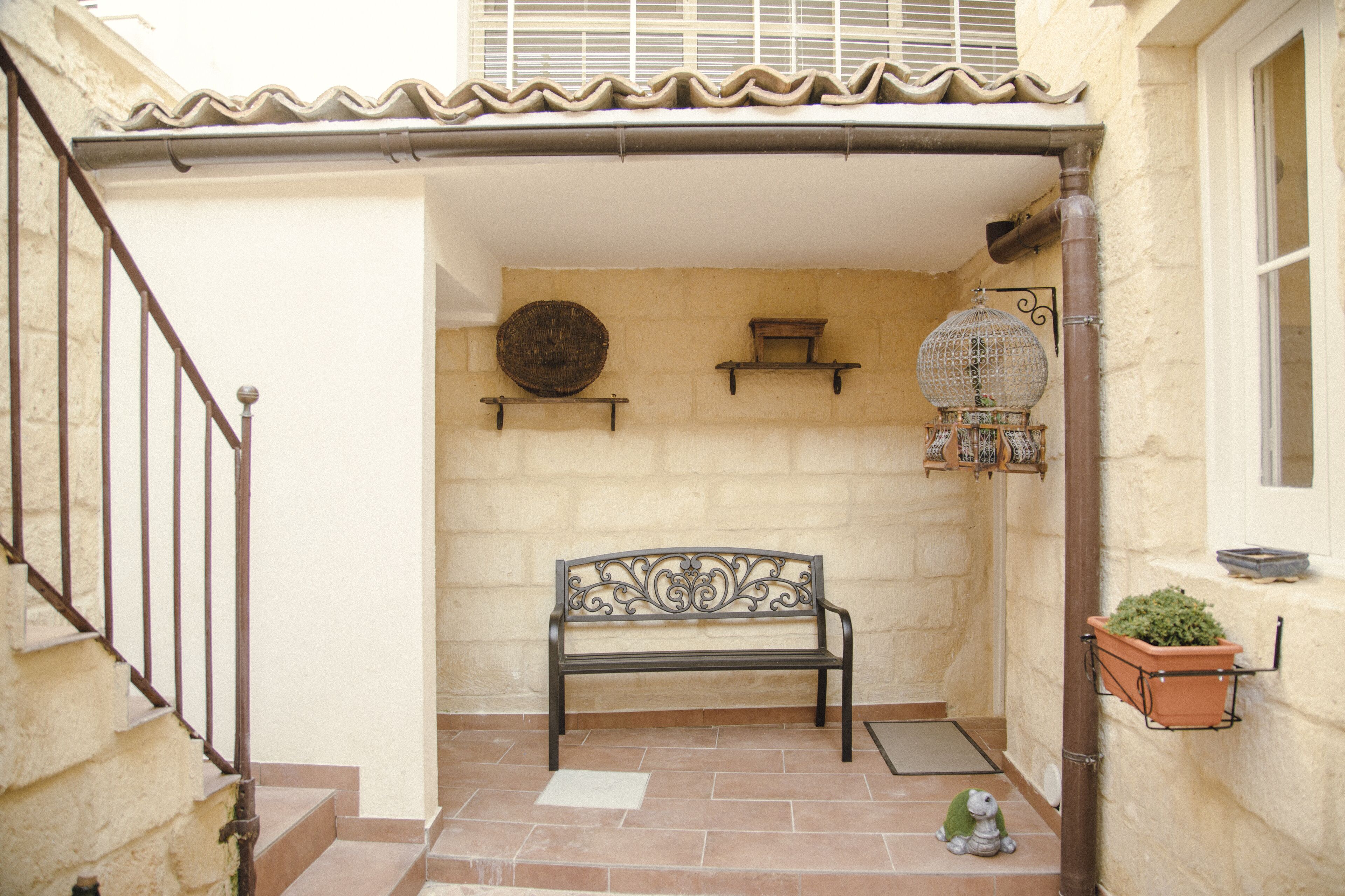 Une cour avec un banc, une petite table et une cage à oiseaux décorative.
