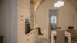 Una cocina moderna con horno empotrado, un comedor con mesa y sillas, y un acceso visible a otra habitación.