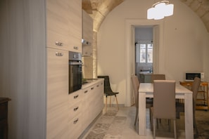 A modern kitchen with a built-in oven, a dining area with a table and chairs, and a unique arched ceiling.
