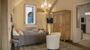 Un dormitorio con una cama, un sillón blanco, un televisor y un guardarropa.