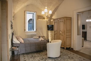 A bedroom with a bed, a chair, a wardrobe, a television, and a window with a view of a building.