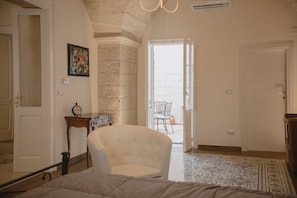 A bedroom with a bed, a chair, a small table, a clock, and a door leading to a balcony.