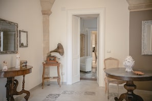 A room with a wooden table, a chair, a small side table, and a mirror on the wall.