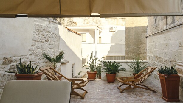 Un patio al aire libre con suelo de baldosas, sillones de madera y plantas en macetas.
