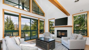 A modern living room with a fireplace, large windows, and a cozy seating area. - Townhome w/ hot tub & AC near village (Whistler)