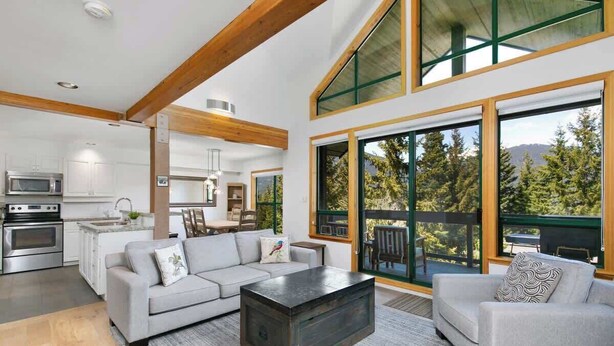 A modern living room with a gray sofa, a coffee table, and a dining area with a table and chairs. - Townhome w/ hot tub & AC near village (Whistler)