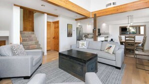 A spacious living area with a grey sofa set, a dark coffee table, and a staircase leading to a wooden loft. - Townhome w/ hot tub & AC near village (Whistler)