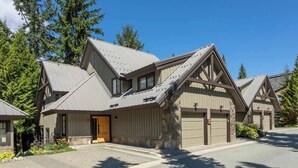 A modern building with a sloped roof, multiple garage doors, and a stone foundation. - Slopeside retreat w/ hot tub & garage (Whistler)