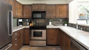 A modern kitchen with wooden cabinets, stainless steel appliances, and a large window providing natural light. - Slopeside retreat w/ hot tub & garage (Whistler)