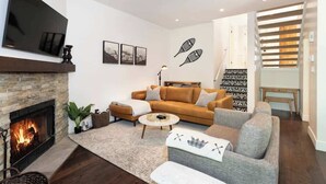A modern living room with a fireplace, a flat-screen TV, a sofa set, and a staircase. - Slopeside retreat w/ hot tub & garage (Whistler)