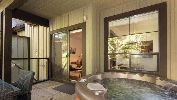 A hot tub on a wooden deck with a glass door leading to a room. - Slopeside retreat w/ hot tub & garage (Whistler)