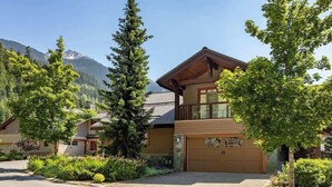 A two-story lodge with a wooden facade, a garage, and a mountain backdrop. - Ski-access retreat w/ hot tub & fireplace (Whistler)