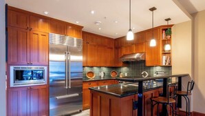 A modern kitchen with wooden cabinets, stainless steel appliances, and a central island with bar stools. - Ski-access retreat w/ hot tub & fireplace (Whistler)