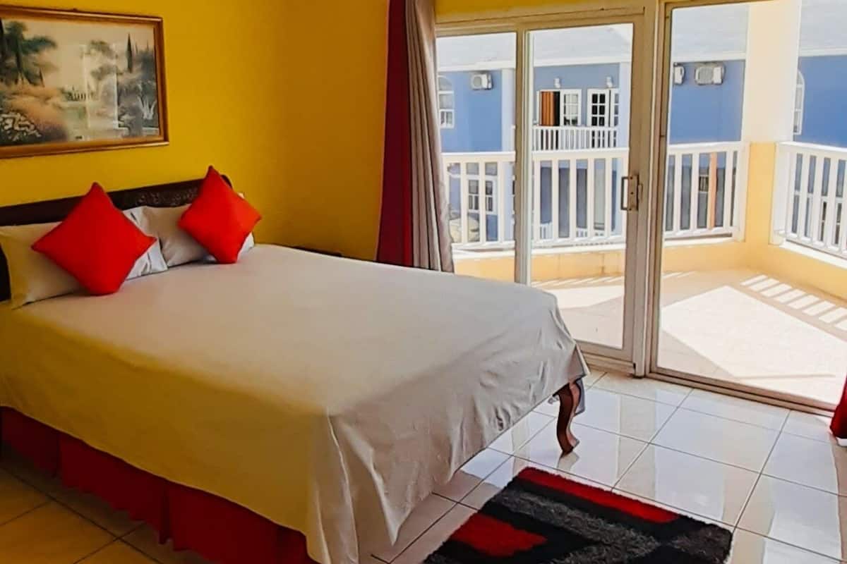 A hotel room with a bed, a painting on the wall, and a view of a blue building through the window.