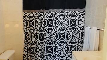 A bathroom with a black and white patterned shower curtain, a toilet with a striped seat, and a white vanity with a mirror.