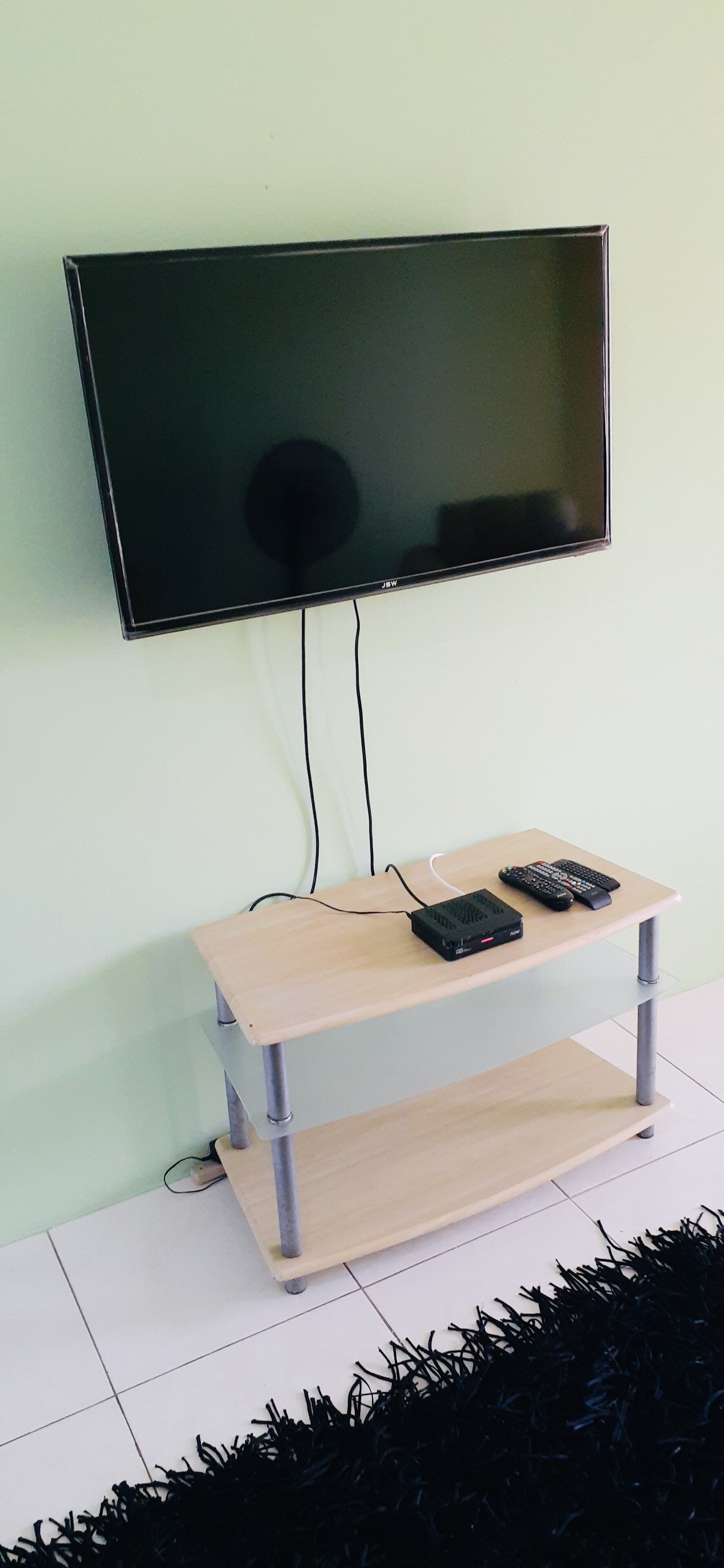 Televisor de pantalla plana montado en una pared sobre un mueble de televisión de madera, con un control remoto y una regleta de enchufes.