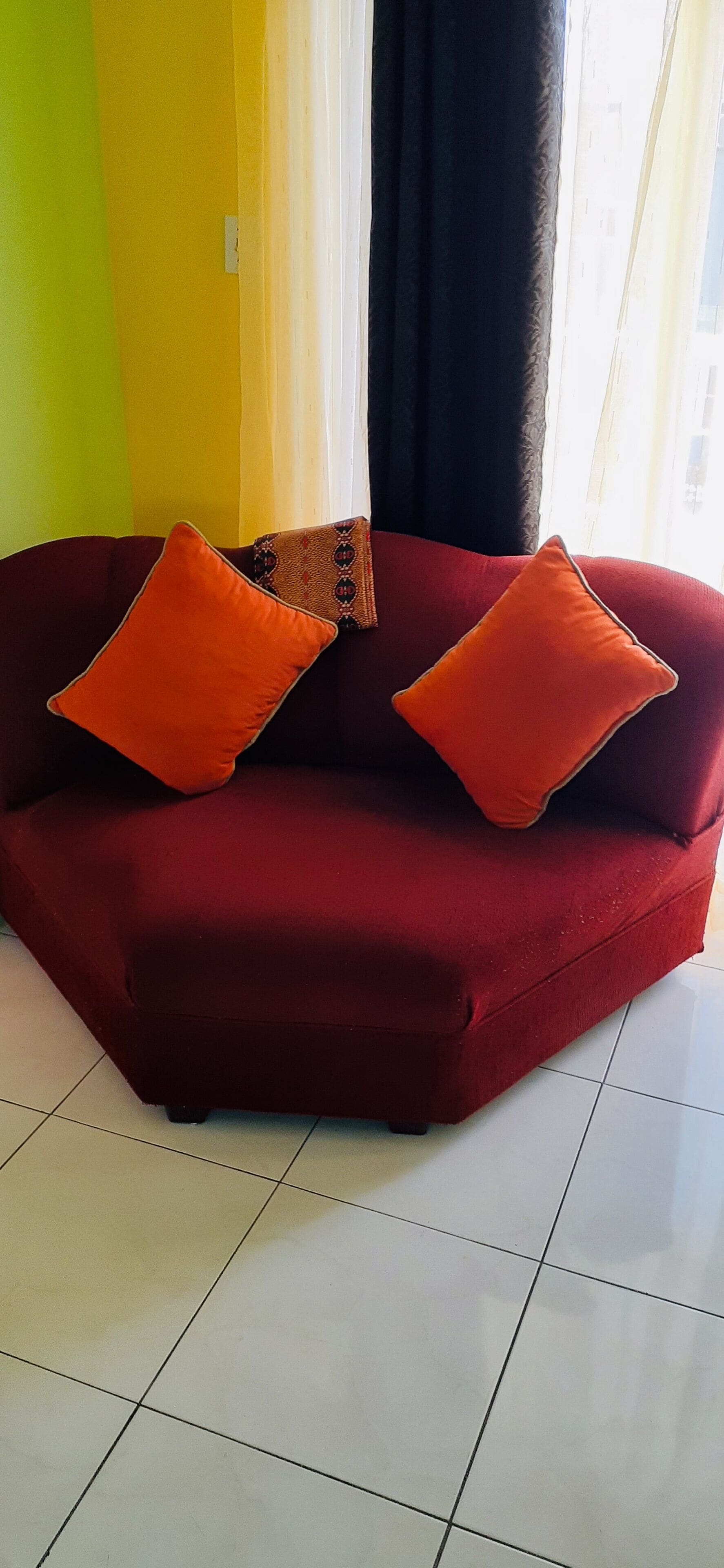 A red sofa with two orange pillows in a room with a tiled floor and a yellow wall.