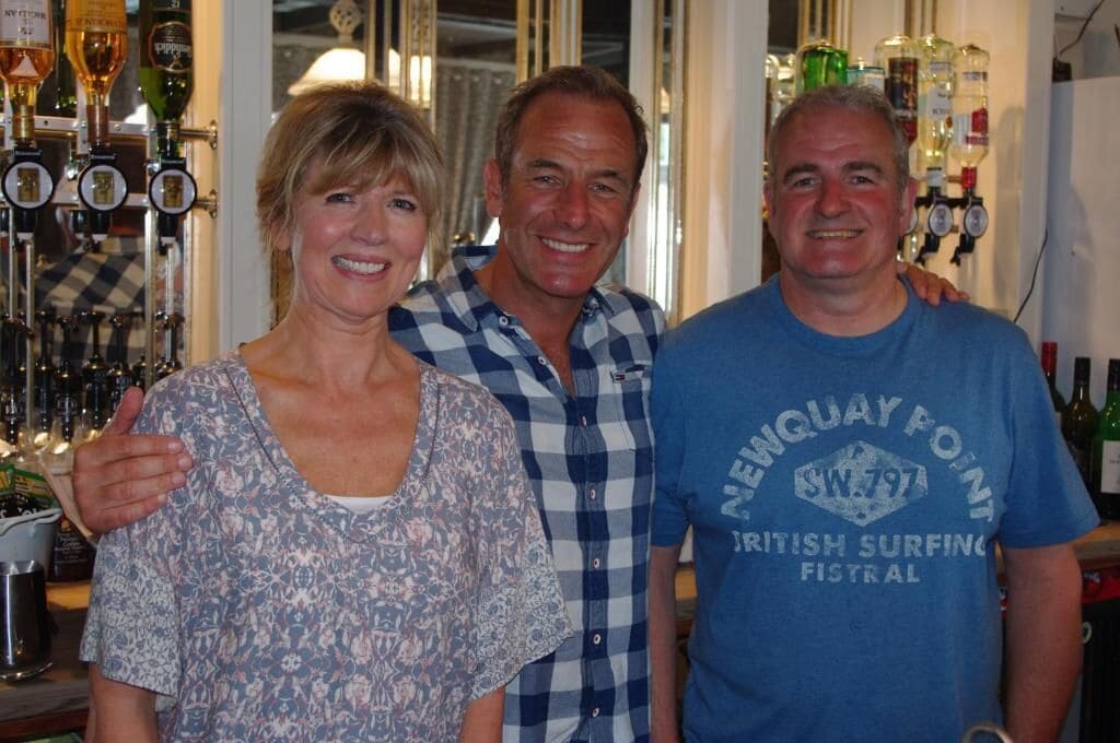 Three people standing in a bar with various bottles and glasses in the background.