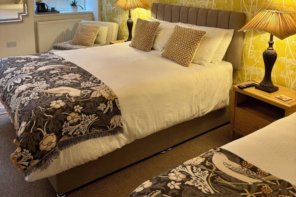 Une chambre à coucher avec un grand lit, des lampes de chevet, une fenêtre avec des stores et un mur orné d’un motif floral.