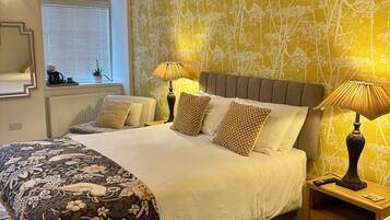 A bedroom with a large bed, bedside lamps, a window with blinds, and a wall with a floral pattern.