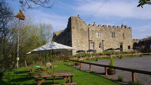 A stone building with a castle-like structure, picnic tables, and umbrellas in a grassy area. - Blenkinsopp Castle Inn (Brampton)