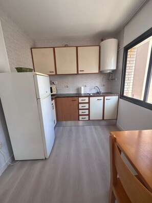 Une cuisine de taille réduite, équipée d’un réfrigérateur, de meubles de rangement en bois, d’un évier et d’une fenêtre.